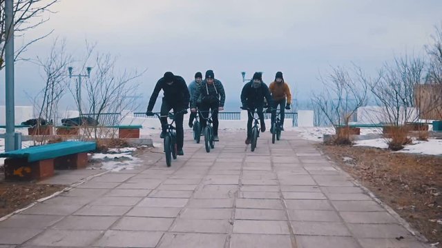 Friends of the teenagers are epically riding together on BMX and doing tricks on a winter day in the park. Slow motion. 120 fps.