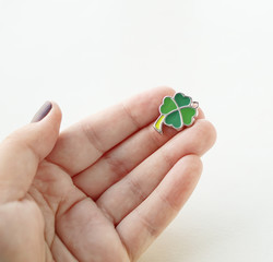 Hand holding a green charm of clover leaf. White background. Focus on clover leaf. Lucky meaning.