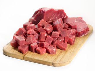 Raw beef piece and slices (cubes) on wooden cutting board isolated on white background