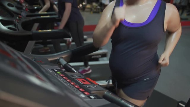 Woman with excess weight running fast on treadmill, working hard for slim body