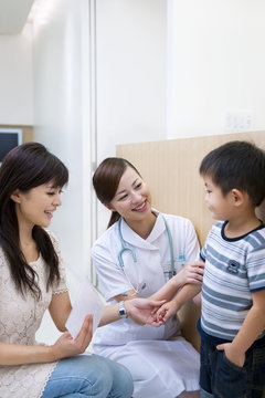 Female Nurse Talking To Boy With Mother At Corridor