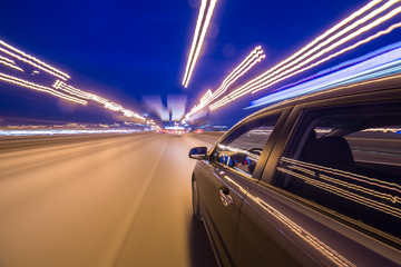 Fototapeta premium View from Side of Car moving in a night city, Blured road with lights with car on high speed. Concept rapid rhythm of a modern city.