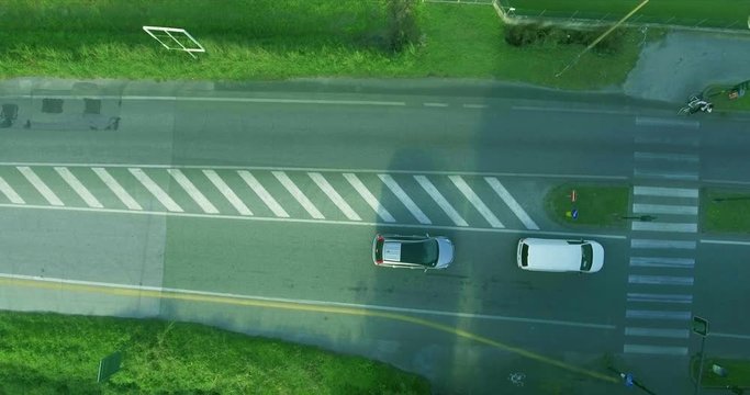 Cars on the road stopped for a red light, skipping the bicyclist. A cyclist crosses the roadway through a pedestrian crossing aerial shot top view