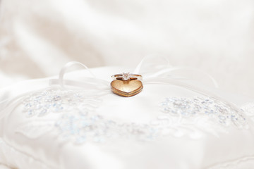 Wedding ring and heart necklace on white pillow 