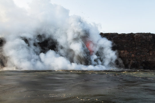 Landscape view of lava entering ocean with explosions, steam and volcanic gases