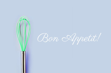 Neon green culinary whisk top view on colorful background. Bon Appetit text. Cook food concept  