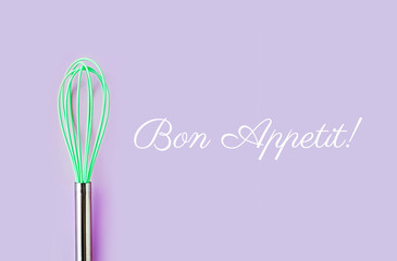 Neon green culinary whisk top view on colorful background. Bon Appetit text. Cook food concept  