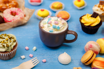 Cupcakes, macaroons and donuts. Mug with whipped cream and marshmallows. Almond macaron cookies. Sweet dessert.