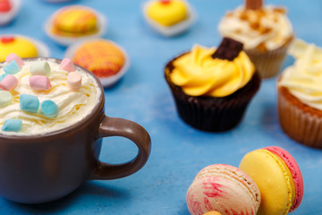 Cupcakes and macaroons cakes. Mug with whipped cream and marshmallows. Almond macaron cookies. Sweet dessert.