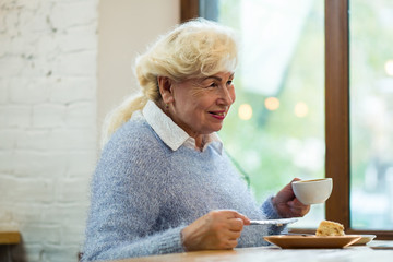 Smiling senior woman holding cup. Cake and coffee. Morning dessert in cafe.