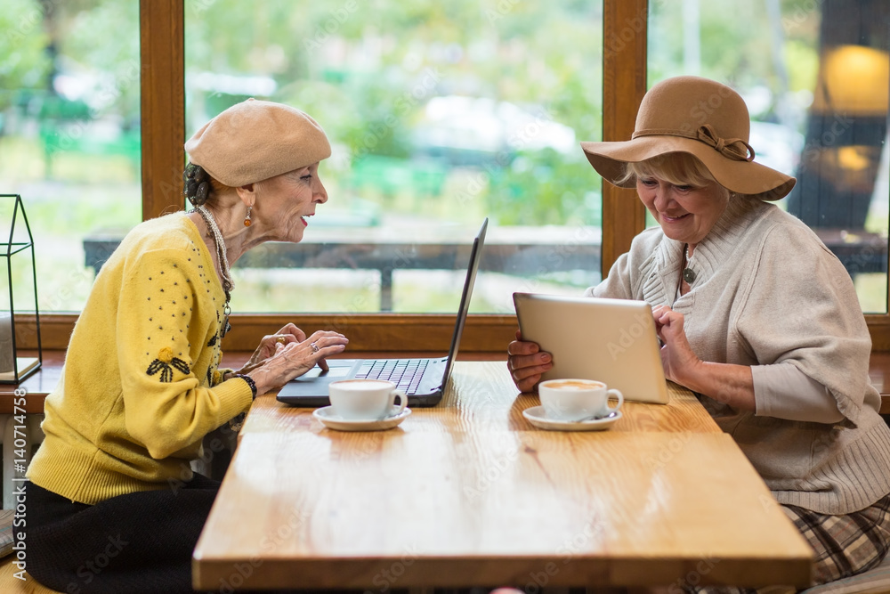 Wall mural senior women sitting in cafe. tablet and notebook pc. features of social networking.