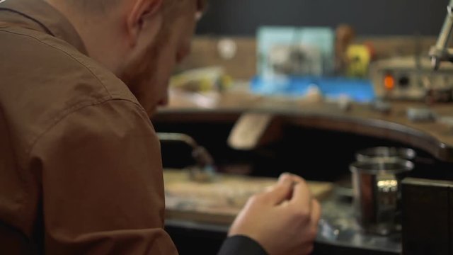 Goldsmith sitting back in a brown shirt and performs soldering silver ring using a blowtorch