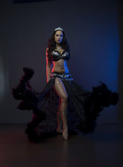 Sexy slim woman, belly dancer in black costume with crystals. Dark background with pink and blue...