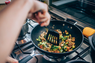 Vegetables being stir fried in wok style pan with spatula on industrial stove top