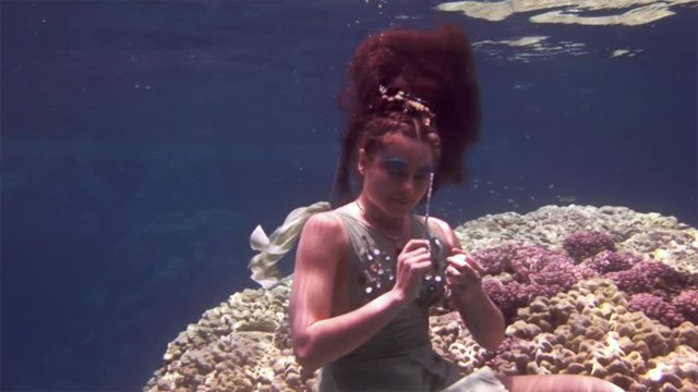 Underwater model free diver swims in clean transparent blue water in Red Sea. Filming a movie. Young girl smiling at camera. Extreme sport in marine landscape, coral reefs, ocean inhabitants.
