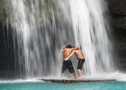 Three men standing under waterfall, Bohol island, Philippines