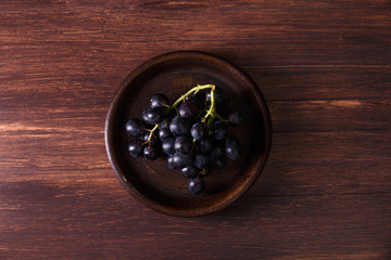 Dark grapes bunch. Ripe grape fruit on rustic plate. On wooden background.