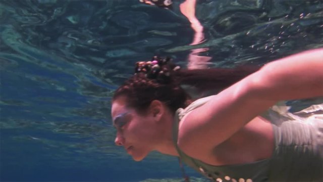 Underwater model free diver in fairy costume on background of corals in Red Sea. Filming a movie. Young girl smiling at camera. Extreme sport in marine landscape, coral reefs, ocean inhabitants.