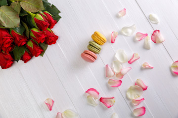 Macaroon cakes with bouquet of red roses. Different types of macaron. Colorful almond cookies. White wooden rustic background.