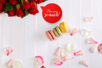 Macaroon cakes with bouquet of red roses. Different types of macaron. I love you speech bubble. White wooden rustic background.