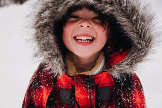 Portrait of a smiling girl standing in the snow wearing a parka coat with a fake fur hood	