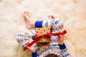 Overhead view of a girl in her pyjamas sitting on the floor opening a wrapped Christmas gift