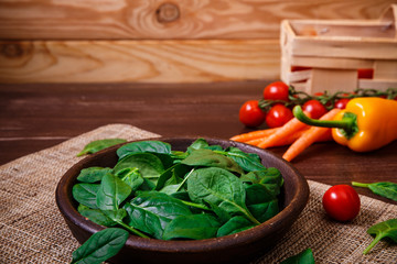 Spinach leaves in bowl. Carrot, pepper and cherry tomatoes. Raw fresh vegetable. Fresh natural plant leaf. Organic food on wooden table.