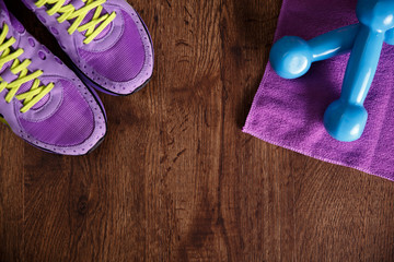 Fitness gym equipment. Sneakers, dumbbells with towel. Workout footwear. Sport trainers on grunge rustic wood background.