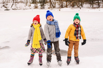 Three children standing side by side on a frozen pond wearing warm winter clothing and ice skates singing Christmas carols
