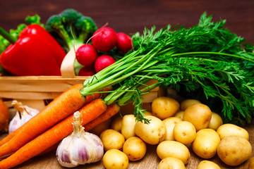 Vegetables. Potatoes, carrot and red pepper. Lettuce salad, garlic and brocoli. Onion and radish. Wooden basket on rustic table.