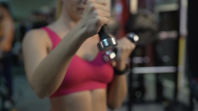 Fit woman doing dumbbell exercises, training in gym for strength and health