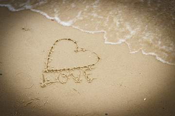 Word love and heart written on sand at the beach by the sea