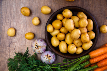 Potatoes in plate. Carrot, garlic and raw new potato. Fresh natural vegetables. Organic bio food on rustic wooden table.