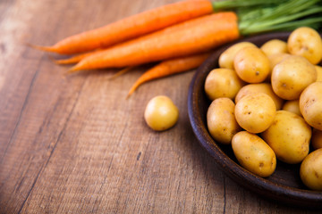 Potatoes in plate. Carrot and raw new potato. Fresh natural vegetables. Organic bio food on rustic wooden table.