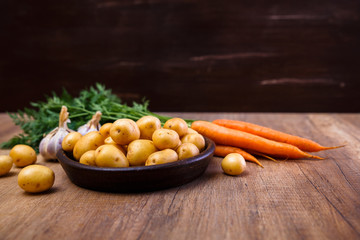 Potatoes in plate. Carrot, garlic and raw new potato. Fresh natural vegetables. Organic bio food on rustic wooden table.