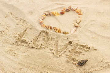 Word love written on sand at the beach, heart of shells