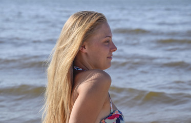 The girl blonde on a background of sea water. Beautiful young woman in a colorful bikini