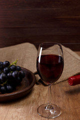 Red wine. Bottle with wineglass. Dark grapes branch on plate. On rustic wooden background.