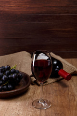 Red wine. Bottle with wineglass. Dark grapes branch on plate. On rustic wooden background.