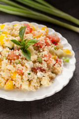Tabbouleh salad with couscous, tomatoes, onion, zucchini and bell peppers topped with basil leaf close up shot