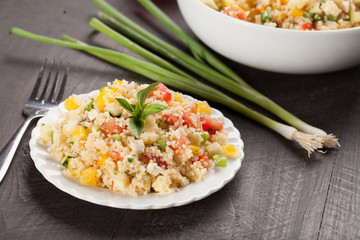 Tabbouleh salad with couscous, tomatoes, onion, zucchini and bell peppers topped with basil leaf with large bowl to side
