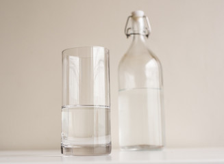 Low angle view of glass of water and bottle on white table (selective focus)