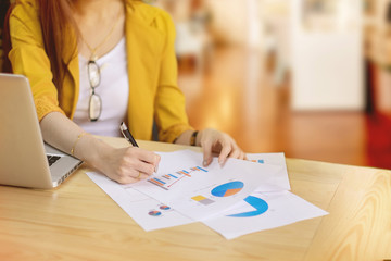 Businesswoman working frame holding pen and paper with charts on wood table in office.