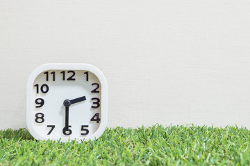 Closeup white clock for decorate show a half past two or 2:30 p.m. on green artificial grass floor and cream wallpaper textured background with copy space