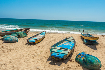 Wide view of group of fishing boats parked alone in seashore with people in the background,...