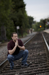 Man crouching to pray on rail road tracks.