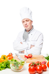 Vertical portrait of a cook at the table with vegetables on a white background