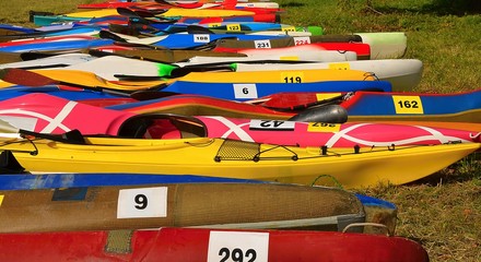 Many colorful kayaks with starting numbers laying on the grass - ready to start race