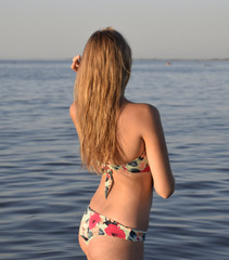 Obraz premium Blond girl in a bikini standing in the sea water. Beautiful young woman in a colorful bikini on sea background