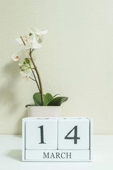 Closeup white wooden calendar with black 14 march word with white orchid flower on white wood desk and cream color wallpaper in room textured background , selective focus at the calendar